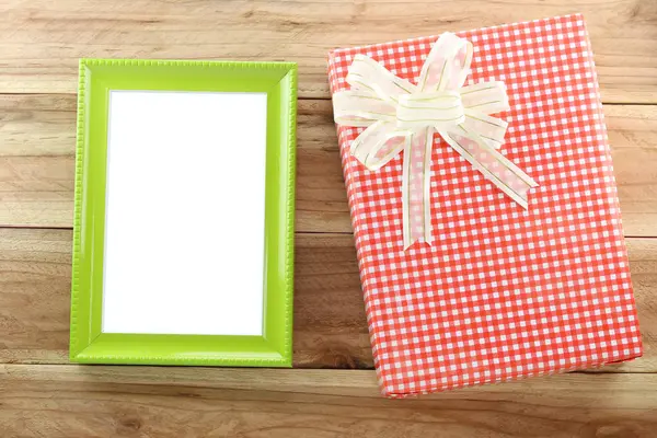 Red gift box with empty wooden picture frame on wood background. — Stock Photo, Image