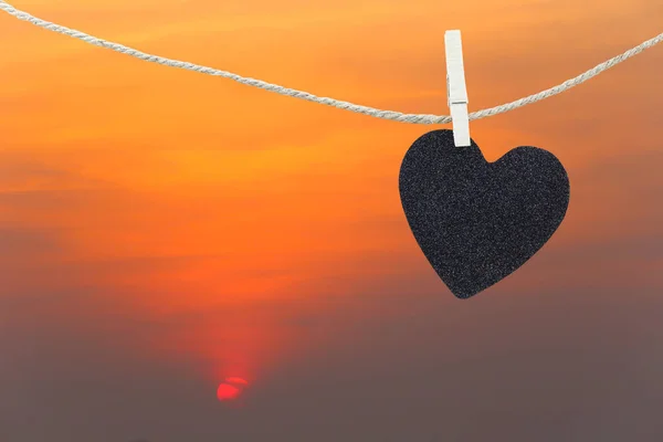 Coração preto pendurado na corda de cânhamo em vista pôr do sol fundo . — Fotografia de Stock