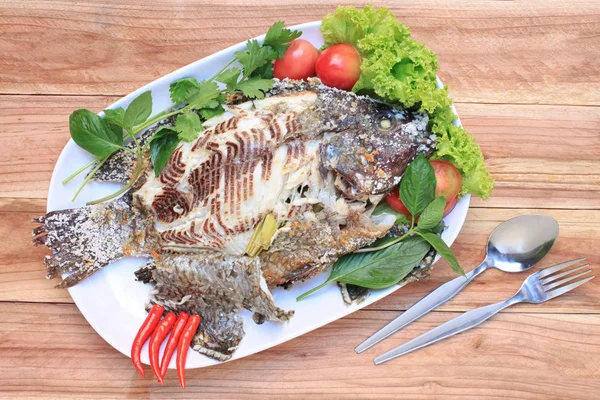 在白盘子里用盐烤的罗非鱼鱼 泰国食物样式放置在木桌上 — 图库照片
