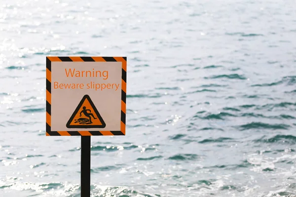 Warning labels of warning beware slippery in seaside area and have sea background.
