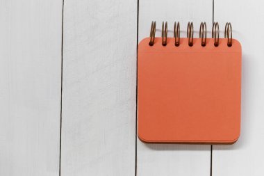 Beyaz ahşap zemin üzerinde boş portakal defter.