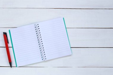 Beyaz ahşap zemin üzerinde kalem ve kitap.