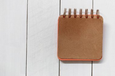 Turuncu defter bir beyaz ahşap zemin üzerinde yer.