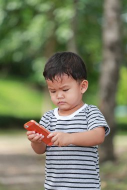 Asyalı çocuk çocuklar yaklaşık iki yıllık bir smartphone bahçede kullanın..