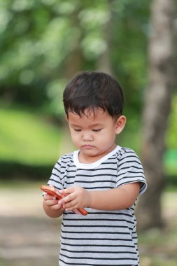 Asyalı çocuk çocuklar yaklaşık iki yıllık bir smartphone bahçede kullanın..