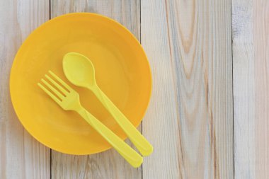 Boş sarı plastik tabak ve kaşık ahşap zemin üzerinde yer.