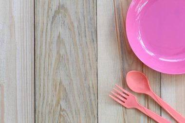 Boş pembe plastik tabak ve kaşık ahşap zemin üzerinde yer.