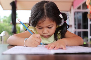 Asyalı çocuk kız eğitim ve öğrenme kavramı kitap üzerinde kalem yazma harfleri kullanın.