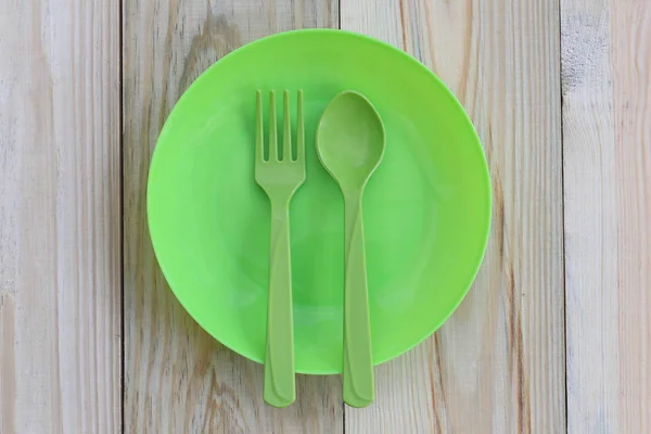 Empty green plastic dish and spoon placed on wooden floor.