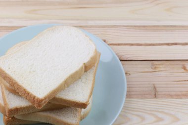 Dilimlenmiş ekmek ahşap zemin üzerinde yeşil tabak içinde yığılmış.