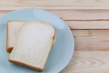 Dilimlenmiş ekmek ahşap zemin üzerinde yeşil tabak içinde yığılmış.
