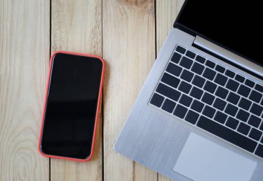 Boş bir akıllı telefon ekranı ve ahşap bir masaya yerleştirilmiş bir laptop..