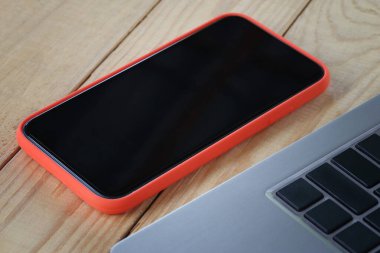 Boş bir akıllı telefon ekranı ve ahşap bir masaya yerleştirilmiş bir laptop..