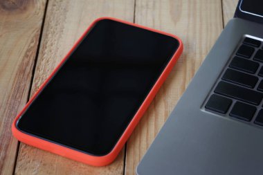 Boş bir akıllı telefon ekranı ve ahşap bir masaya yerleştirilmiş bir laptop..