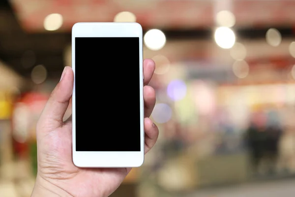 Hand av en man som innehar smartphone-enhet i Blur shopping mal — Stockfoto