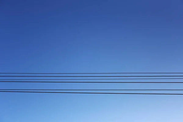 Kabeldraden van de elektrische polen op blauwe lucht achtergrond. — Stockfoto