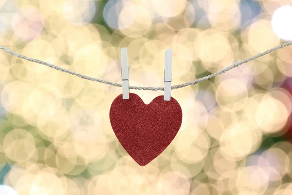 Corazón rojo colgando de una cuerda de cáñamo en el fondo bokeh oro . — Foto de Stock