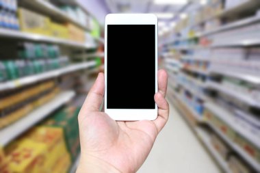 Alışveriş merkezinin arka planında akıllı telefon cihazı tutan ve ekranında beyaz fotokopi alanı olan bir adamın eli..