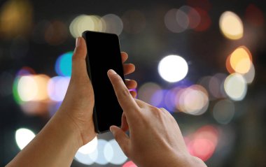 A man's finger pointing to the empty black screen of smartphone on a dark bokeh background.