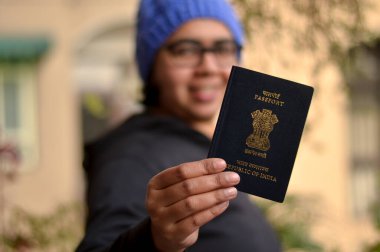 Pasaportunu yüzünde bulanıklıkla tutan mavi şapkalı güzel bir Hintli kadının portresi. Konsept, kışın uluslararası bir tatile çıkmaya hazır mutlu bir yolcuyu tasvir ediyor.