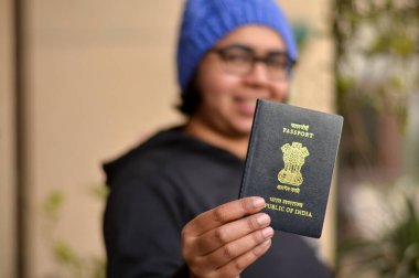Pasaportunu yüzünde bulanıklıkla tutan mavi şapkalı güzel bir Hintli kadının portresi. Konsept, kışın uluslararası bir tatile çıkmaya hazır mutlu bir yolcuyu tasvir ediyor.