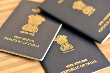 Birçok (üç) Hint pasaportu sergilenmekte olan ahşap arka planda tutuluyor. Hindistan Cumhuriyeti 'nin ulusal amblemi, Sarnath' lı Ashoka 'nın aslan başkentidir. Küresel vatandaş