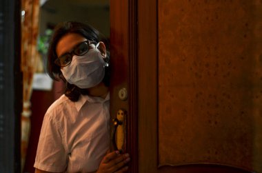 Ev karantinası altında endişeli ve endişeli bir kadın grip ve Coronavirus (Covid-19) salgınına karşı koruyucu solunum maskesi takıyor ve evine gelen ziyaretçiyi karşılıyor.