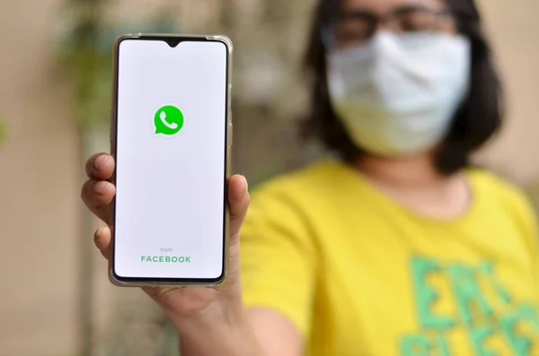 Yeni Delhi, Hindistan, 2020. Maskeli kız Whatsapp uygulamasını cep telefonunda Corona virüsü (Covid-19) salgını için evde karantina altında gösteriyor. Whatsapp tüm nesiller arasında çok yaygın bir mesajlaşma uygulamasıdır.