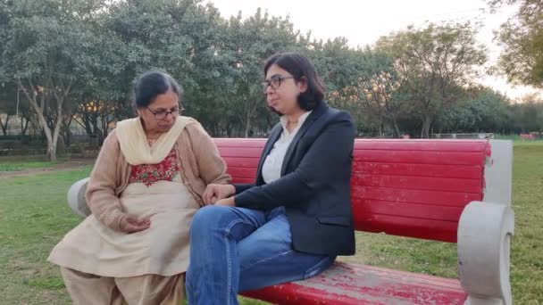 赤ベンチでピーナッツを剥離し それらを食べて 法律で彼女の娘と公園に座って引退したインドの女性のショット コンセプト Happy Rechire Life — ストック動画