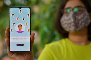 Delhi, Hindistan, 2020. Aarogya Setu uygulamasını cep telefonunda karantina altında gösteren maskeli bir kız. Corona virüsü (Covid-19) salgınının önlenmesi ve test edilmesi için Hint govt 'u tarafından başlatılır.