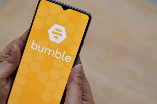Londra, İngiltere, İngiltere, 2020. Düz zemin, tahta arka plan ve Bumble uygulaması logosu kadın ellerindeki akıllı telefon ekranında sergileniyordu. Bumble bir çevrimiçi sosyal arama ve flört mobil uygulaması