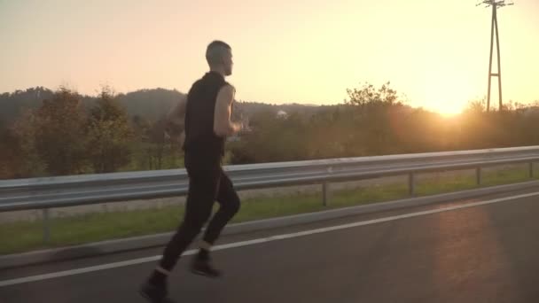 4kフォロービデオの若いですフィット男ジョギングで夕日,屋外で路上 — ストック動画