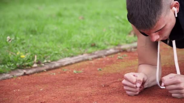 4k opløsning closeup pan bevægelse video af unge fit mand laver planke motion om morgenen udendørs på løbebanen – Stock-video