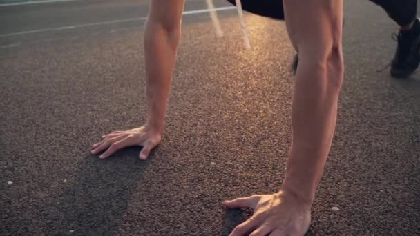 4k pan beweging video van jonge fitte man doen push-ups in de avond buiten op de weg bij zonsondergang met sterke zon vlam — Stockvideo