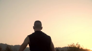 Gün batımında açık havada egzersiz yapmadan önce bir adamın siluetinin 4 km çözünürlüğü egzersizlerle ısınması.