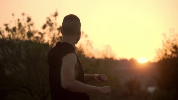 4k felbontása egy férfi bemelegítő gyakorlatok előtt intenzív edzés szabadban naplementekor a természetben — Stock videók