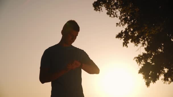 Bir adamın silueti arka planda güzel bir günbatımında akıllı saatlere dokunup kontrol ediyor. — Stok video