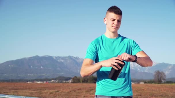 Resolución 4k de un joven en forma preparando batido de proteínas y bebiéndolo con montañas por la espalda — Vídeo de stock