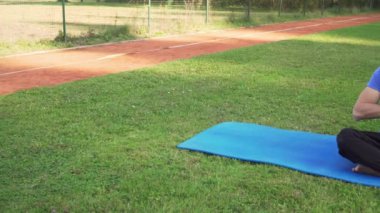 4K çözünürlüklü spor giyen genç bir adamın parkta oturup yoga yapması.