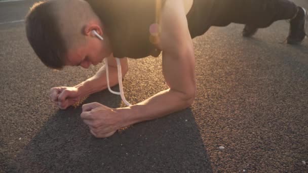 4k rozdzielczość pan ruch młody fit człowiek robi ćwiczenia deski w godzinach porannych na zewnątrz na torze wyścigowym — Wideo stockowe