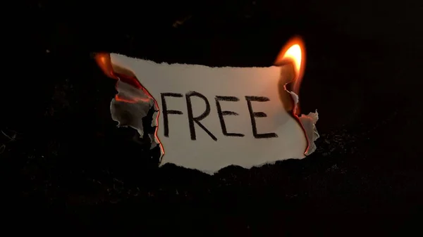 Palabra gratuita escrita en papel blanco quemaduras. Fuego con humo y cenizas sobre fondo negro — Foto de Stock