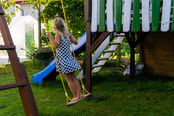 Chica rubia de 3-5 años divirtiéndose en un columpio al aire libre. Parque infantil de verano. Chica balanceándose alto. Niño pequeño en columpio en el jardín — Foto de Stock