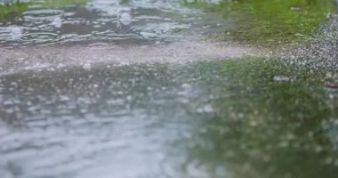 Slow Motion Close 4k: yağmur damlaları asfaltta büyük bir su birikintisine dökülüyor, sokakları sel basıyor. Yağmur mevsiminde sağanak yağmur nedeniyle yollar taşar. Su altındaki yola düşen yağmur damlaları