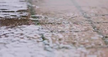 Slow Motion Close 4k: Yağmur damlaları kaldırımlardaki büyük su birikintilerine dökülüyor, sokakları sel basıyor. Şiddetli yağmur mevsiminde yol taşkınları.