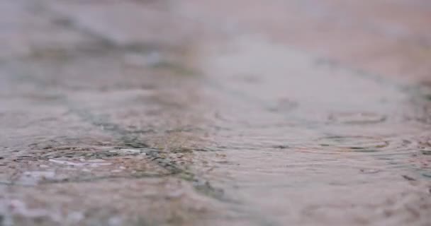 SLOW MOTION CHIUDI 4K: gocce d'acqua piovana cadono in una grande pozzanghera sulle pavimentazioni, inondando la strada. Inondazioni stradali a causa delle forti piogge nella stagione umida . — Video Stock
