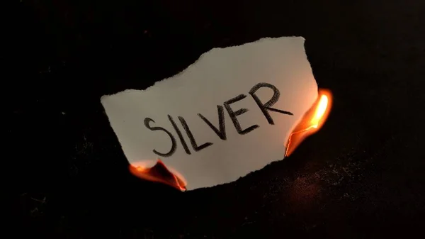 Palavra de prata escrita em queimaduras de papel branco. Fogo com fumaça e cinzas no fundo preto — Fotografia de Stock