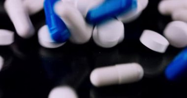 White and blue medical pills falling on a black background