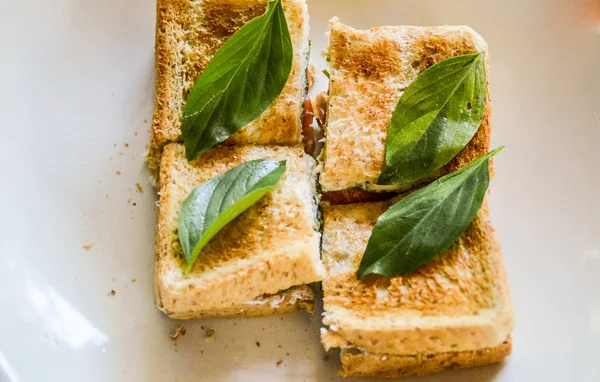 Peynirli tost ve beyaz tabakta fesleğen yaprağı. en üstteki görünüm.