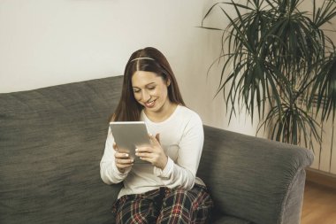 Evde tabletini kullanan genç bir kadın.