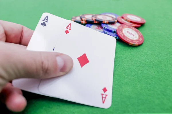 Elinde yeşil bir masada iki as ve poker fişi olan iki kart var.